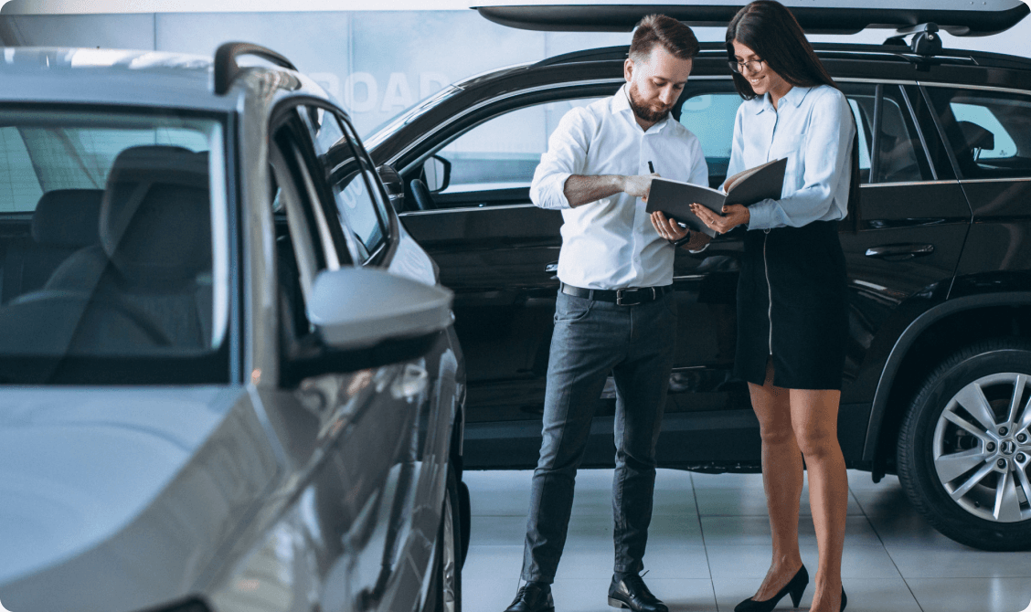 Two dealership colleagues reviewing paperwork together on a showroom floor