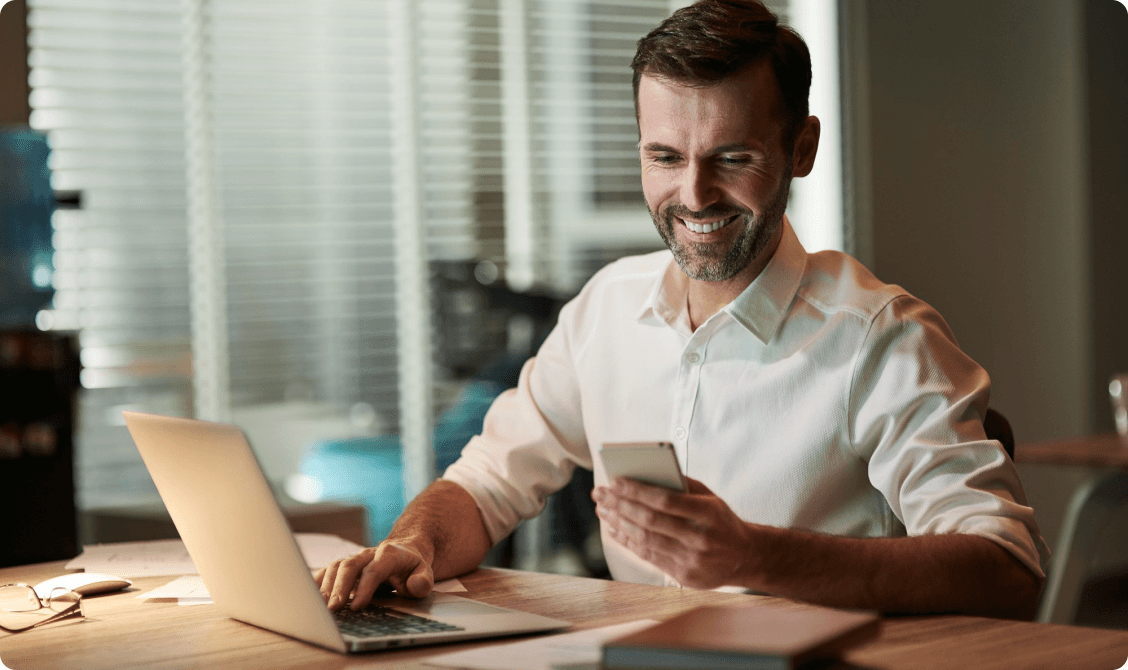 Dealer catching up on industry news from a laptop and phone at his desk